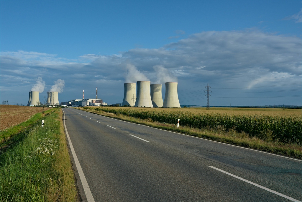 Kraftwerk mit rauchenden Kühltürmen neben einer Straße im ländlichen Gebiet.